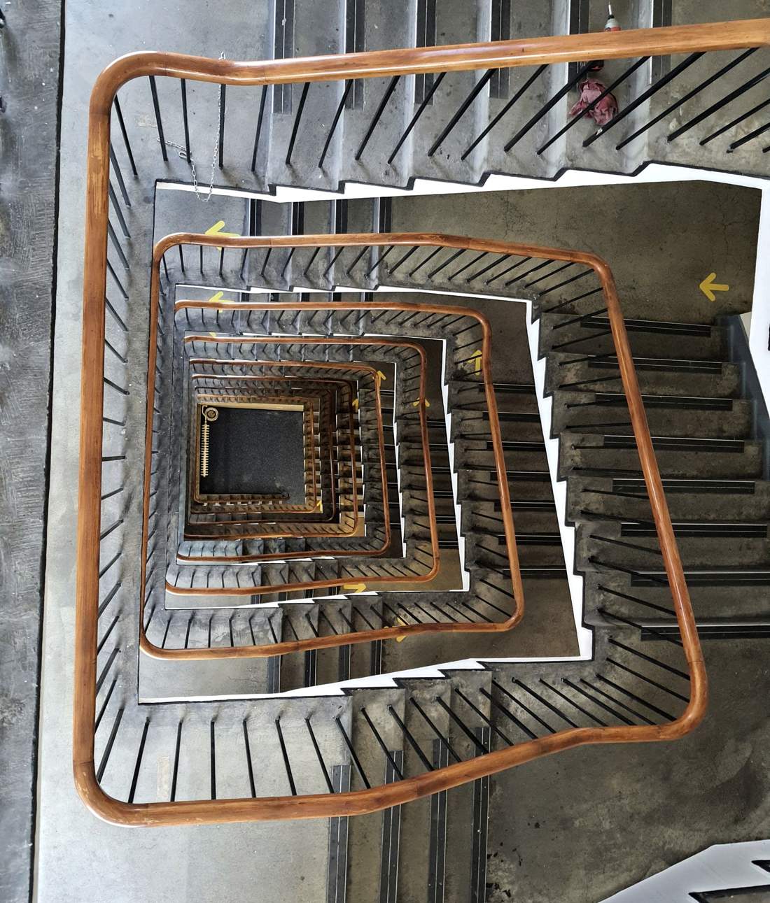 Looking straight down a concrete stairwell with orange handrails, five floors deep